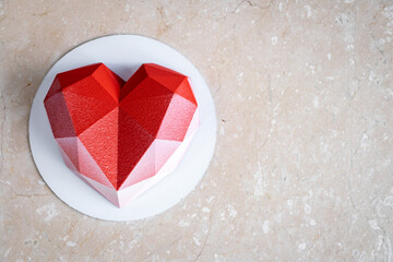 Faceted red heart mousse cake with velor coating on a soft pink marble table, top view. Copy space