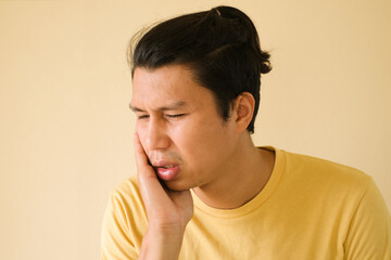 A man in yellow T-shirt holding his cheek with hand, suffering from painful toothache. Tooth decay or sensitivity. Dental health and care concept