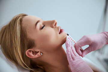 Professional cosmetologist injecting a dermal filler into the patient lips - obrazy, fototapety, plakaty
