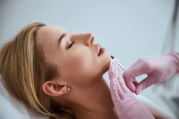 Fotobehang Professional cosmetologist injecting a dermal filler into the patient lips © Viacheslav Yakobchuk