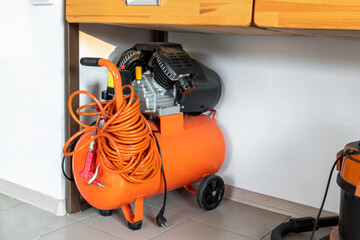 Orange small portable industrial power air compressor with coil hose and pneumatic gun at home...