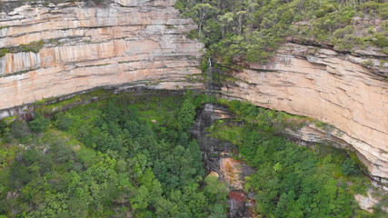 Waterfall in the middle of a cliff, around green trees. Blue Mountains National Park.