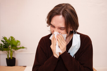 A man sneezes, a medical mask. Empty space for text on a white background. A sick man in home...