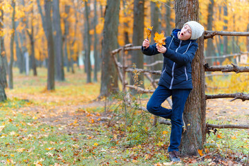 a girl posing near wooden fence and enjoys autumn in city park, beautiful nature with yellow leaves