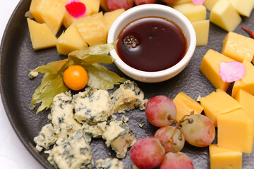 cheese plate with different cheese slices, grapes,   honey