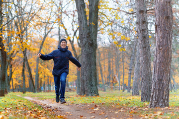 a boy running through the park and enjoys autumn, beautiful nature with yellow leaves