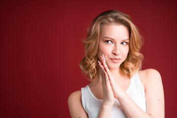 Fototapeta premium Portrait of woman with blond curly hair in white tank top showing praying gesture on red background.