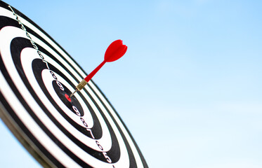 Red target board and darts behind a blue sky, goal setting concept to achieve business results.