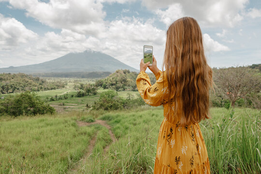 Woman taking picture of Agung volcano on Bali island, Indonesia. Travel and blogging concept. Back view.