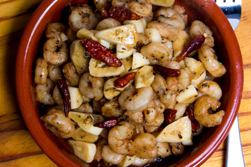 Prawns with garlic and cayenne in a ceramic bowl on a wooden tray