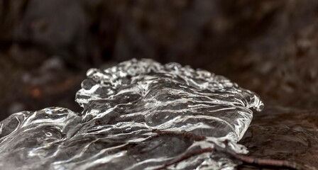 A piece of ice frozen on a tree branch close-up against the dark water of a fast river in early...