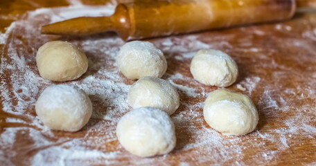 Dough balls, wooden rolling pin and wheat flour on a wooden cutting Board close-up