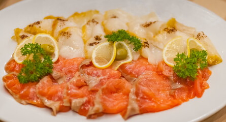 Sliced red salmon and white oily fish decorated with lemon wedges, dill sprigs and green olives on a white ceramic plate close-up