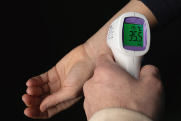 Digital thermometer gun for checking measurement shows 35.5 degrees of body temperature in girl or woman © Olya