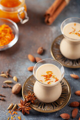 Golden Cinnamon Saffron Almonds Milk. Golden milk with species cardamom, turmeric, cinnamon, honey and ginger on wooden background. Trendy hot Healthy Vegan Drink. Indian Garam Badami Doodh.