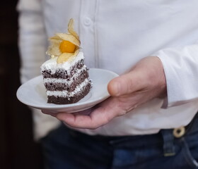 A piece of cake on a white ceramic plate in the hands of a man close up