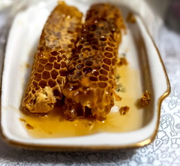 A piece of honeycomb with honey on a white ceramic plate close-up on a tablecloth background