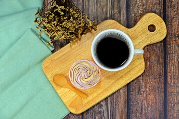 Homemade cupcake served on wooden cutting board with a cup of black coffee and wooden spoon on wooden table.