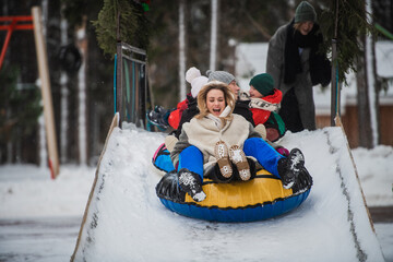 Mother, father, son and daughter ride in winter from an ice slide on a multi-colored tubing.