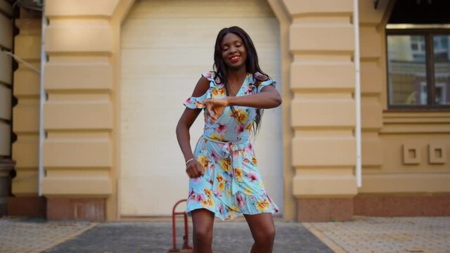 Smiling afro girl dancing bachata in city. African woman moving body on street