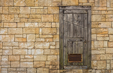 Fototapeta na wymiar Old rectangular yellow dry stone wall with wooden door. The style is an ancient Roman architecture.