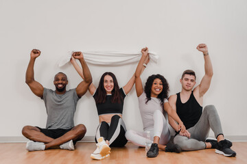 Cheerful smiling mixed-race people posing with raised hands and towel in gym