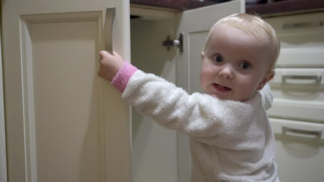 baby opens the kitchen cupboard,baby playing in the kitchen opens and closes the cupboard