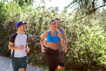 Group of young people in sports clothing running in city park.