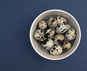 The quail eggs in the ceramic bowl on the dark background. Flat view. Closeup.