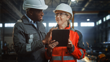 Two Heavy Industry Engineers Stand in Steel Metal Manufacturing Factory, Use Digital Tablet...