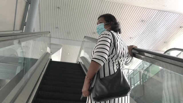 Asian businesswoman wearing face mask using the escalator, going up a building.