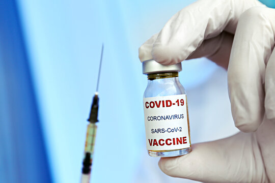 Macro shot of doctor's hands in blue latex gloves showing the new covid-19 vaccine vial and suringe filled with medicine. Close up, copy space, background.