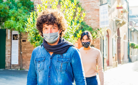 Group Of Latino Curly Man And A Brunette Woman Wearing Protective Face Mask After Lockdown Reopening. Young Couple Walking On Urban Street Keeping Social Distance Outdoor In Winter. New Normal Life