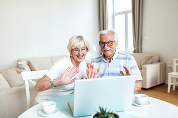 Obraz premium Senior couple is talking online via video connection on the laptop. Having nice time withfriends and family via video call waving on the camera