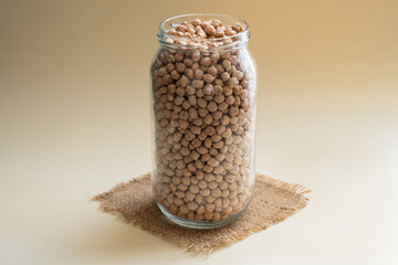glass jar with chickpeas and old burlap fabric napkin rough linen jute, sackcloth piece isolated on white beige background