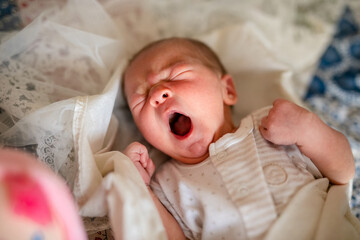 Newborn baby for the first time at home, lying in a blanket on the bed, smiling, yawning, pulling pens, falling asleep, baby's morning, baby products concept.