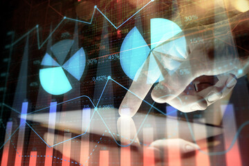 Double exposure of man's hands holding and using a digital device and forex graph drawing. Financial market concept.