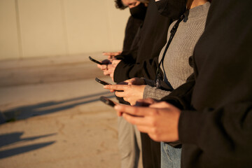 Hands of a group of friends using a smart phone. They are dressed in black and gray, without any color in the scene.