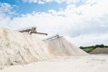 Stone crushing conveyor belt equipment and huge piles of crushed limestone against a blue sky in...
