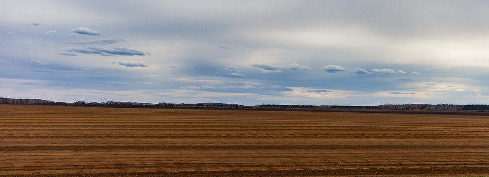 Arable land and cloudy grey sky with clouds in spring