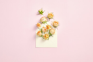 Rose flowers in paper envelope on pastel pink background. Flat lay, top view. Stylish composition with gift for Mothers Day, Valentine Day, birthday. Minimal style.