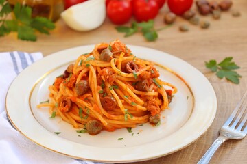Italian Traditional Dish"Spaghetti al Tonno" or "Spaghetti with Tuna",spaghetti with tuna in olive oil,tomatoes sauce,onions,olives,capers,parsley and peppers on plate with wooden table background