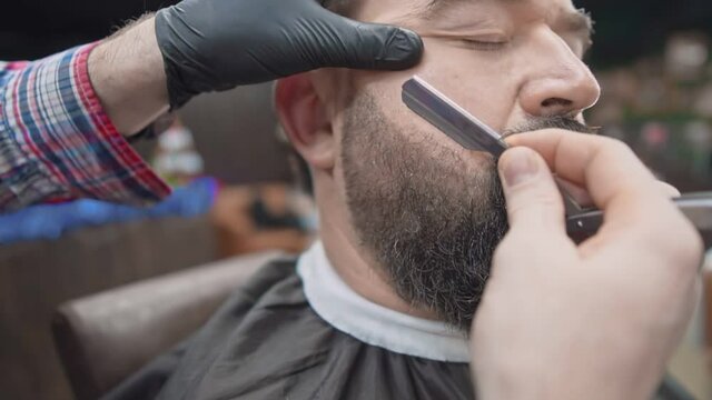 The barber carefully shaves beard with a straight razor