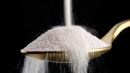 pouring collagen powder in golden spoon on black background closeup. Natural beauty and health...