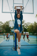 Beautiful woman holds on with hands and hangs on basketball hoop.