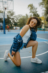 Beautiful young woman poses among basketball playground.