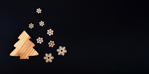 The zero waste new year concept as a handmade wooden fir tree with the falling snowflakes on the black background, banner.