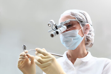 Dentist in a protective screen and a medical mask on his face. Binocular glasses. Prevention of caries and gum diseases.