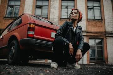 Obraz na płótnie Canvas Young woman sits on street near red retro car.