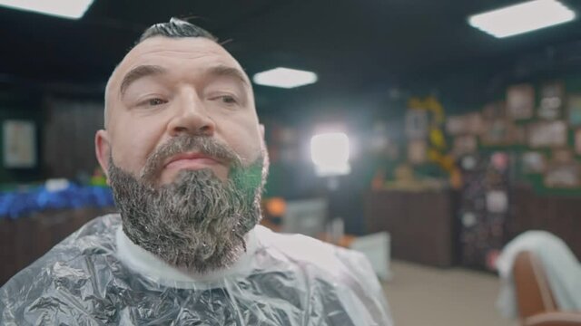 A man sits in a barber's chair dyeing his beard